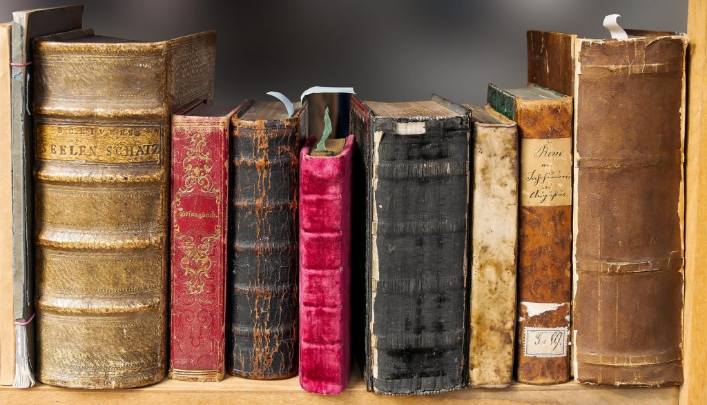 Foto van allemaal hele oude boeken die er beetje beschadigd eruit zien op een rijtje op een plank